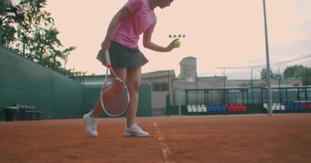 Låg vinkel vy i slow-motion av en ung kvinnlig tennisspelare förbereder sig för att tjäna en tennismatch. En kvinnlig idrottsman slår kraftfullt en boll under idrottsträningen. Filmklipp för kommersiellt bruk — Stockvideo