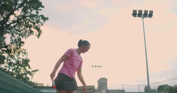 Vista de ángulo bajo en cámara lenta de una joven jugadora de tenis que se prepara para servir un partido de tenis. Una atleta está golpeando poderosamente una pelota durante la práctica deportiva. Material de uso comercial — Vídeos de Stock