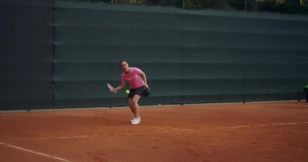 Επαγγελματική εξοπλισμένη γυναίκα χτυπάει σκληρά την μπάλα του τένις με ρακέτα τένις. Γυναίκα τενίστρια σε δράση κατά τη διάρκεια του παιχνιδιού. Φοράει μη επώνυμα αθλητικά ρούχα.. — Αρχείο Βίντεο