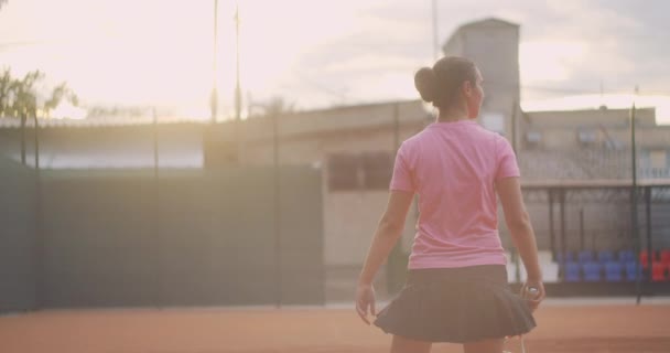 Uma morena cansada jogadora de tênis caminha ao longo da quadra de tênis se recuperando e concentrando. Intervalo numa partida de ténis. Jogador de tênis após a partida no mapa ao pôr do sol em câmera lenta. — Vídeo de Stock