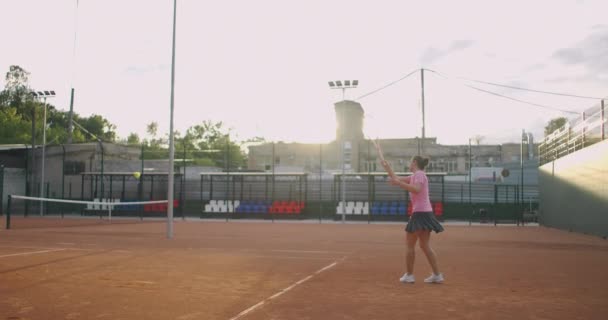 Młoda kobieta przechodząca przez kort tenisowy z rakietą. Widok z tyłu atrakcyjnej brunetki w niebieskiej koszuli i czarnych spodenkach wchodzących w kort tenisowy. Pełna długość następnie strzał z miejsca kopiowania — Wideo stockowe