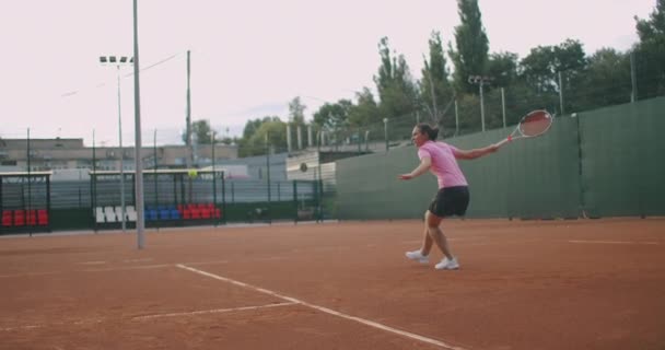 Бічний вид на молоду кавказьку жінку, яка грає в теніс на корті, повертаючи м "яч у повільному темпі. — стокове відео
