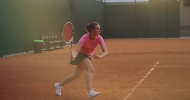 A young brunette tennis player plays a ball at sunset on a tennis court. A woman plays tennis professionally and dynamically in slow motion — Stock Video