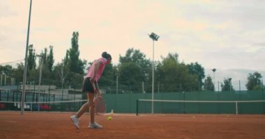 Slow Motion tenis kortu ağındaki tenis antrenmanının ticari görüntüleri. Tenis oynayan bir bayan sporcunun düz görüntüsü. Genç bir sporcu spor eğitiminde topa vuruyor.