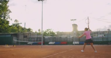 Genç bir kadın tenis kortunda raketle yürüyor. Mavi gömlekli ve siyah şortlu çekici esmer kadın tenis kortuna giriyor. Kopyalama alanı ile tam uzunluk takip çekimi