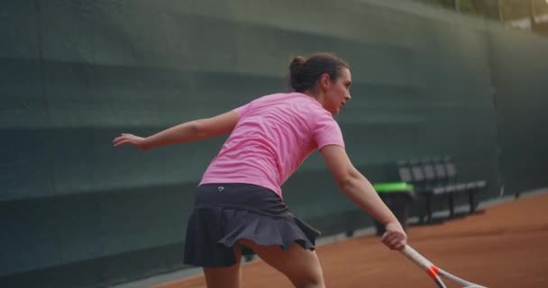 Mladý brunetka tenista hraje míč při západu slunce na tenisovém kurtu. Žena hraje tenis profesionálně a dynamicky ve zpomaleném filmu — Stock video