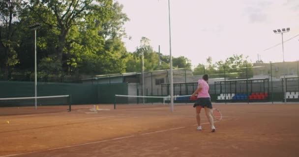 Mujer joven caminando por la cancha de tenis con raqueta. Vista trasera de atractiva morena femenina en camisa azul y pantalones cortos negros entrando en pista dura de tenis. Longitud completa seguir tiro con espacio de copia — Vídeos de Stock