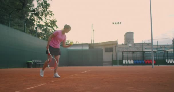 若い選手のスローモーション側のビューは、テニスボールの奉仕を訓練します。10代の選手がコートでテニスをしている。現役女子はスポーツ練習中に力強くボールを打っている — ストック動画