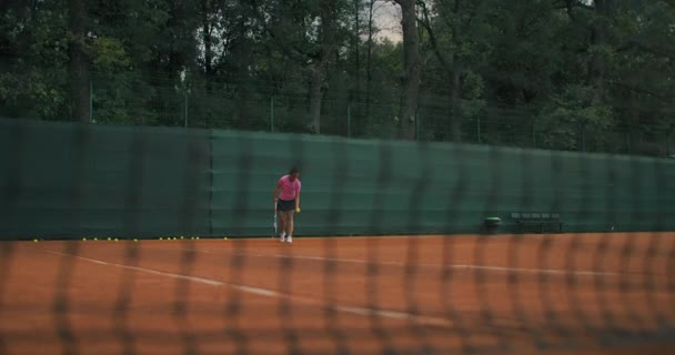 Vista lateral en cámara lenta de un joven atleta entrena el servicio de la pelota de tenis. Un atleta adolescente está jugando tenis en una cancha. Una chica activa está golpeando poderosamente una pelota durante la práctica del deporte — Vídeos de Stock