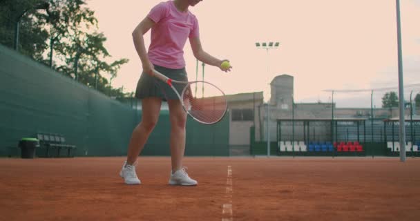 Zeitlupe: Sportlerin beim Training. Eine Großaufnahme einer Sportlerin dient dem Tennisball. Junge Frau schlägt bei Sonnenuntergang mit ihrem Tennisschläger auf den Ball ein — Stockvideo