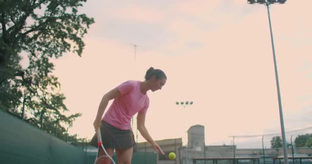 Zwolniony ruch: kobieta sportowiec podczas jej praktyki. Zbliżenie dziewczyny sportowca serwuje piłkę tenisową. Młoda kobieta uderza piłkę rakietą tenisową o zachodzie słońca — Wideo stockowe