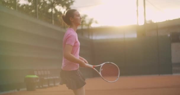 Une jeune joueuse de tennis brune joue une balle au coucher du soleil sur un court de tennis. Une femme joue au tennis professionnellement et dynamiquement au ralenti — Video
