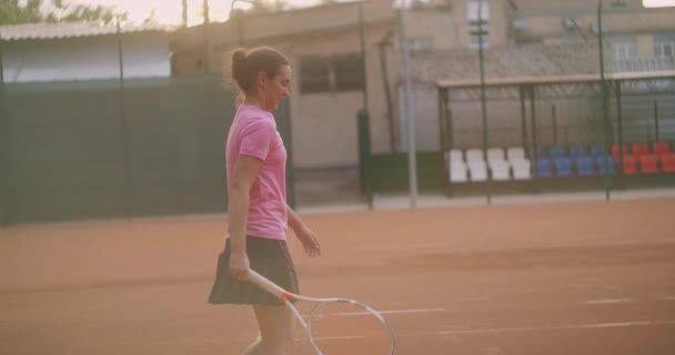 Zmęczona brunetka tenisistka spaceruje po korcie tenisowym, dochodząc do siebie i koncentrując się. Przerwa w meczu tenisowym. Tenisista po meczu na mapie o zachodzie słońca w zwolnionym tempie. — Wideo stockowe