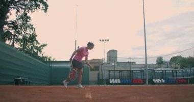 Yavaş çekim: kadın sporcu antrenman sırasında. Bir kız sporcunun yakın çekimi tenis topunu servis eder. Genç bir kadın gün batımında tenis raketiyle topa vuruyor.