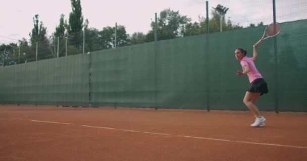 Fiatal női teniszező koncentrál és összpontosít a kézügyességre. Szakmai felszerelt női verte keményen a tenisz labdát tenisz ütő. — Stock videók