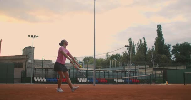 Slow-motion zijaanzicht van een jonge atleet traint het dienen van de tennisbal. Een tiener atleet speelt tennis op een veld. Een actief meisje slaat krachtig een bal tijdens het sporten — Stockvideo