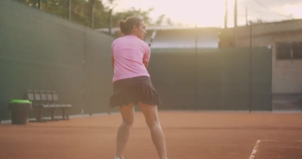 Mujer joven caminando por la cancha de tenis con raqueta. Vista trasera de atractiva morena femenina en camisa azul y pantalones cortos negros entrando en pista dura de tenis. Longitud completa seguir tiro con espacio de copia — Vídeos de Stock