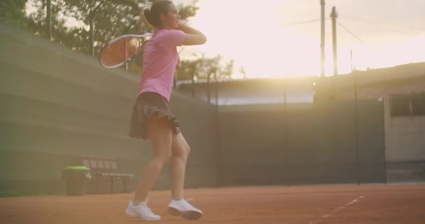 Mujer joven caminando por la cancha de tenis con raqueta. Vista trasera de atractiva morena femenina en camisa azul y pantalones cortos negros entrando en pista dura de tenis. Longitud completa seguir tiro con espacio de copia — Vídeos de Stock