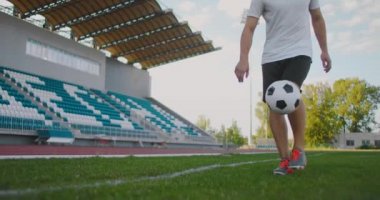 Futbol sahasındaki profesyonel erkek futbolcu spor ekipmanlarıyla ağır çekimde bir futbol topuyla jonglörlük yapıyor. Stadyumda elinde top olan bir futbolcu ayakta duruyor.
