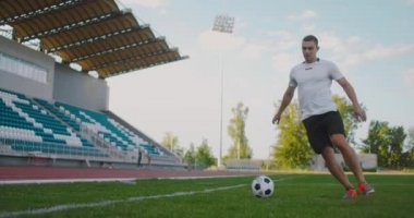 Stadyumdaki futbol sahasında futbol topuyla koşan bir erkek futbolcunun yakın çekimi mükemmel top sürüşü ve top kontrolünü gösteriyor..