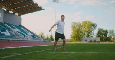 Üniformalı profesyonel bir futbolcu, tribünlerin yanındaki futbol sahasında takım arkadaşından pas alır ve topu sahada kaçırır.