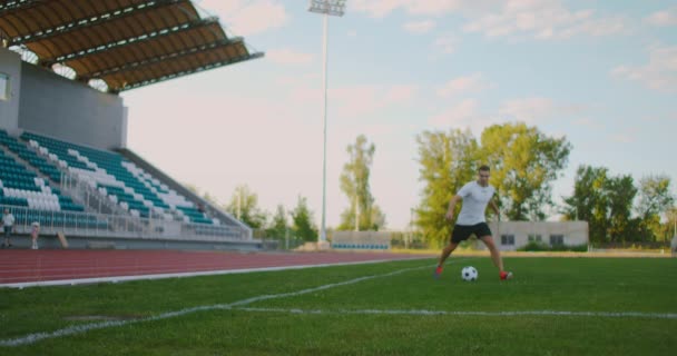 Un jugador de fútbol profesional en uniforme en el campo de fútbol del estadio hace una patada en el balón después de una carrera exitosa con la pelota a lo largo del borde — Vídeos de Stock