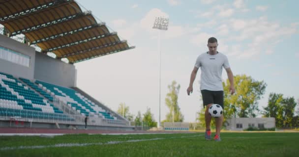 Profissional Atleta jogador de futebol masculino no campo de futebol em câmera lenta em equipamentos esportivos malabarismos uma bola de futebol. Um jogador de futebol com uma bola no estádio perto das arquibancadas de manutenção — Vídeo de Stock