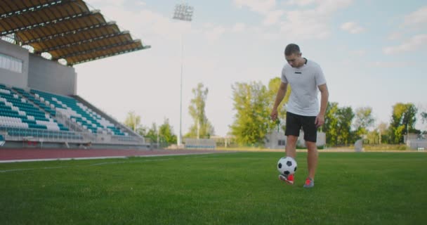 Человек на футбольном поле в замедленной съемке в спортивном снаряжении отскакивает от футбольного мяча — стоковое видео