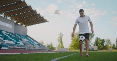Futbol sahasındaki profesyonel erkek futbolcu spor kıyafetleri içinde bir futbol topuyla yavaş çekimde hokkabazlık yapıyor.