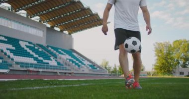 Futbol sahasındaki profesyonel erkek futbolcu spor ekipmanlarıyla ağır çekimde bir futbol topuyla jonglörlük yapıyor. Tribünlerin yanındaki stadyumda topu olan bir futbolcu.