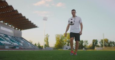 Profesyonel futbol ligindeki ağır çekimde, güneşli bir yaz gününde sahada top bacağında hokkabazlık yapan erkek.