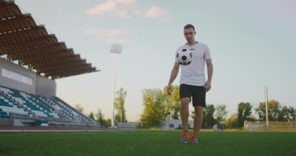 Profesyonel futbol ligindeki ağır çekimde, güneşli bir yaz gününde sahada top bacağında hokkabazlık yapan erkek. — Stok video