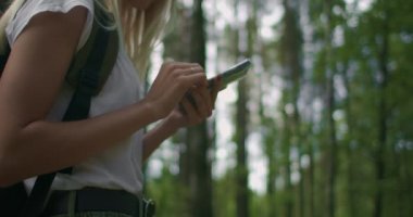 Elinde cep telefonu olan bir kadının ormanda ağır çekimde sırt çantasıyla dolaşırken görüntüsü. Cep telefonunuzdaki Navigator 'u kullanarak ormanda gezinin.