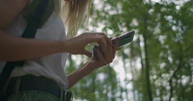 Elinde cep telefonu olan bir kadının ormanda ağır çekimde sırt çantasıyla dolaşırken görüntüsü. Cep telefonunuzdaki Navigator 'u kullanarak ormanda gezinin.