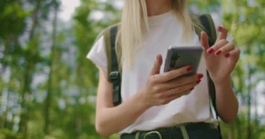 Ormanda yürüyen bir kadın yolcunun elindeki cep telefonunun yakın çekimi. Sosyal ağlar seyir subayı ve ulak. Ormanda yürümek için cep telefonunu kullan.