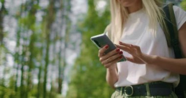 Ormanda yürüyen bir kadın yolcunun elindeki cep telefonunun yakın çekimi. Sosyal ağlar seyir subayı ve ulak. Ormanda yürümek için cep telefonunu kullan.