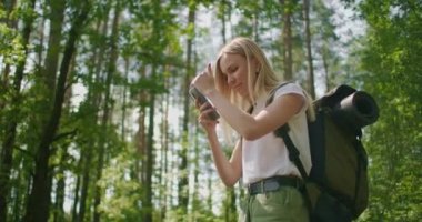 Ormanda sırt çantalı bir gezgin yol boyunca yürür ve cep telefonu ekranına bakar.