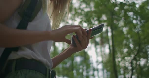 Detailní záběr ženy držící mobilní telefon kráčející lesem s batohem v pomalém pohybu. Navigace lesem pomocí Navigátoru v mobilním telefonu — Stock video