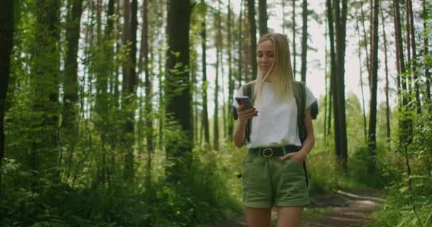 Donna attraente rilassarsi nella foresta e utilizzando smartphone all'aperto. Donna che cammina nella foresta e digita il messaggio sullo smartphone. Escursionista solista femminile con smartphone. — Video Stock