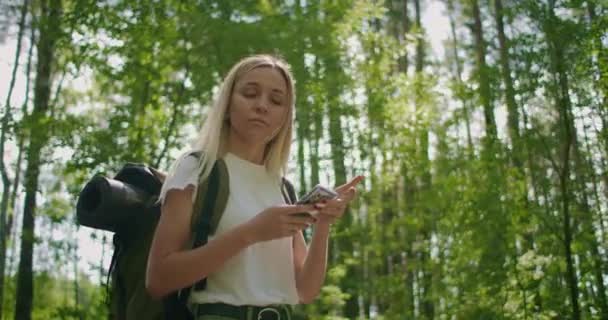 Un viaggiatore nella foresta con uno zaino cammina lungo il percorso e guarda lo schermo del telefono cellulare — Video Stock