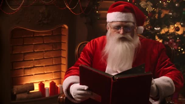 Santa Claus sedí doma u vánočního stromku a odpočívá u krbu. — Stock video