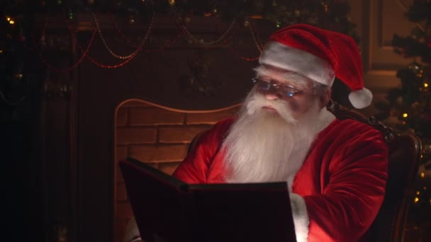 Święty Mikołaj siedzi w domu na wygodnym krześle i czyta list — Wideo stockowe