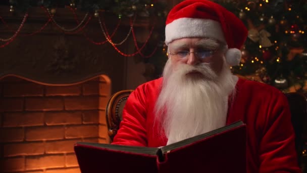 Santa Claus sedí doma u vánočního stromku a odpočívá u krbu. — Stock video