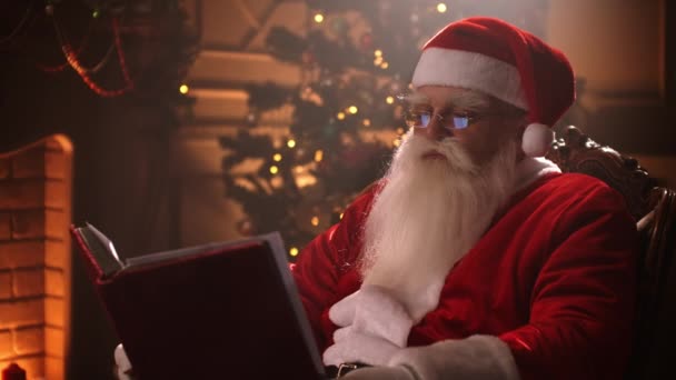 Санта Клаус сидит у себя дома в удобном кресле и читает письмо — стоковое видео