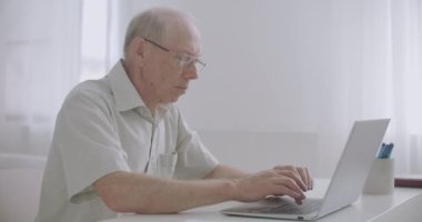 Yaşlı adam uzaktan çalışıyor, e-posta ile mesaj yazıyor ve gönderiyor, dizüstü bilgisayarını kullanıyor, evde kalıyor