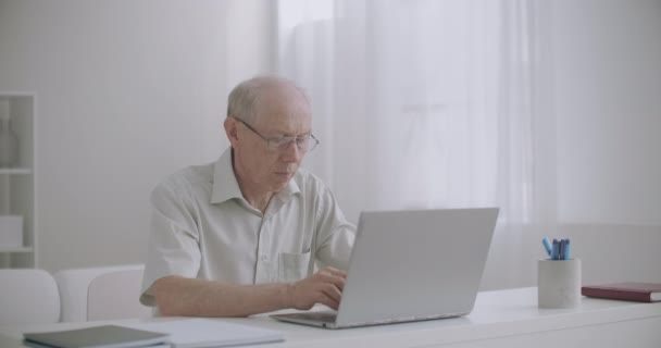 Ηλικιωμένος άνδρας ελεύθερος επαγγελματίας εργάζεται από το σπίτι με το lap-top, ηλικιωμένος συγγραφέας γράφει το βιβλίο, πληκτρολογώντας το κείμενο στο πληκτρολόγιο — Αρχείο Βίντεο