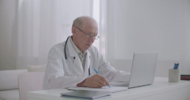 Médico masculino está lendo artigo científico na tela do notebook, navegar na internet para educação e treinamento avançado — Vídeo de Stock