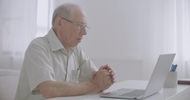 Hombre anciano especialista experimentado se está comunicando por videollamada en el ordenador portátil con sus colegas, trabajando desde casa — Vídeos de Stock