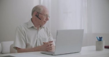 Yaşlı adam not defterine video kullanıyor, evde oturuyor, iş arkadaşlarıyla iletişim kurmak için, kendi kendini izole eden ve uzaktan çalışan