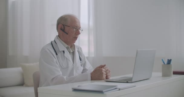 高齢者の経験豊富な男性医学教授はオンラインでオフィスに座って学生に教えています — ストック動画